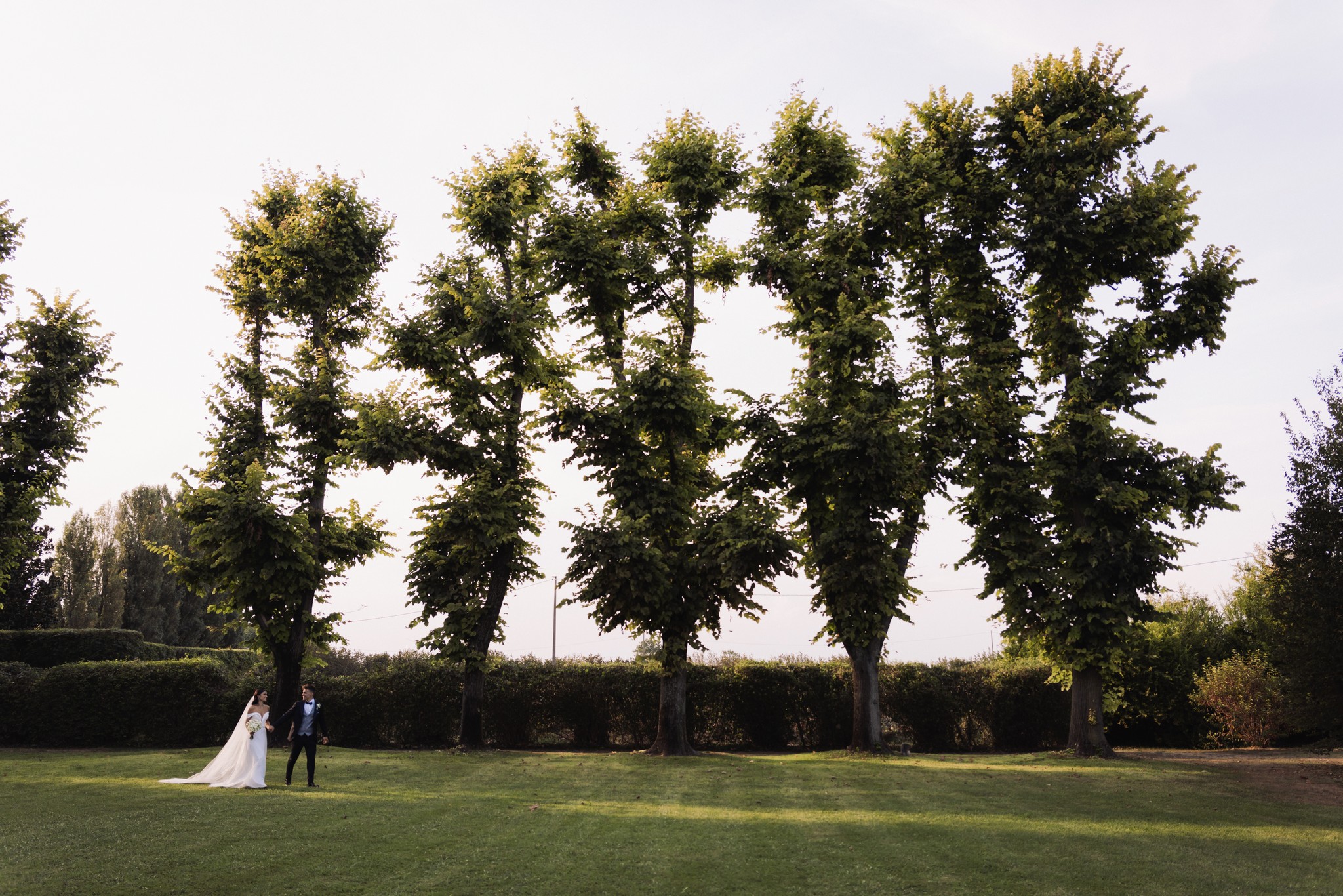 Sposi su prato verde davanti a alberi monumentali a Villa Negri, reportage matrimoniale con luce naturale pomeridiana