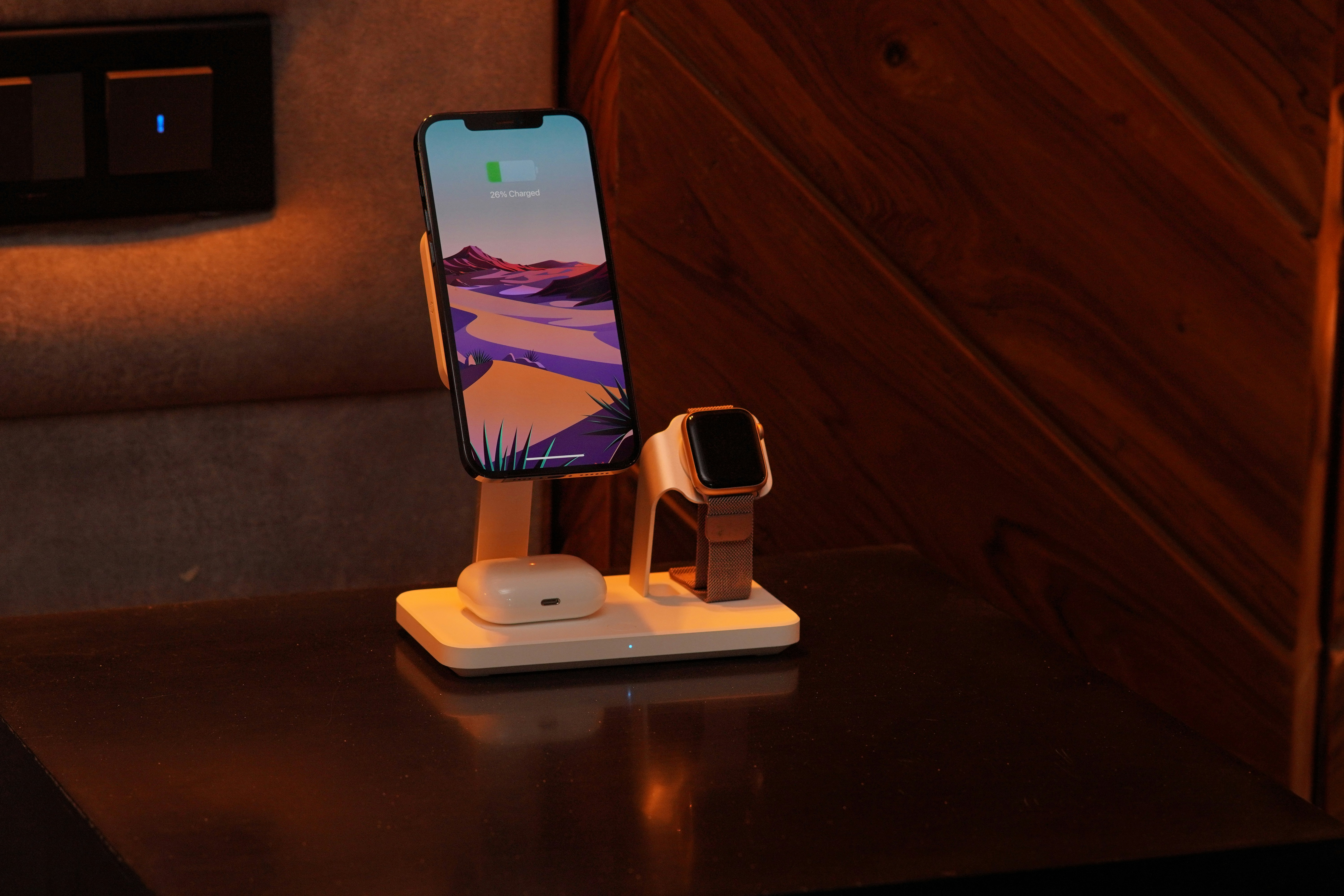 Three-in-one charging dock on a wood nightstand charging an iPhone, Apple Watch, and AirPods