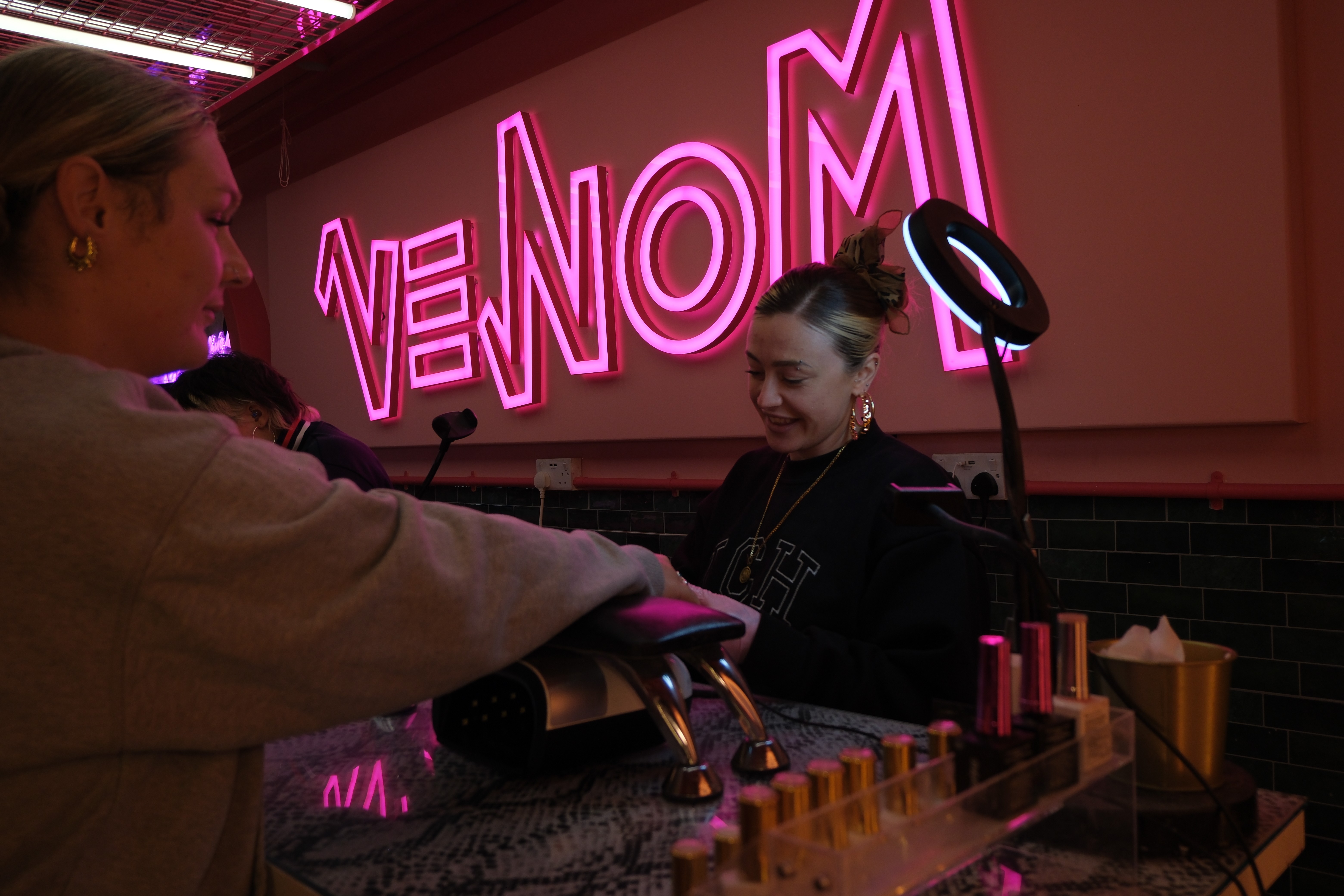 A close-up side profile of a technician wearing a navy athletic jacket, smiling and focused while holding a client’s hand over a snakeskin-print desk.