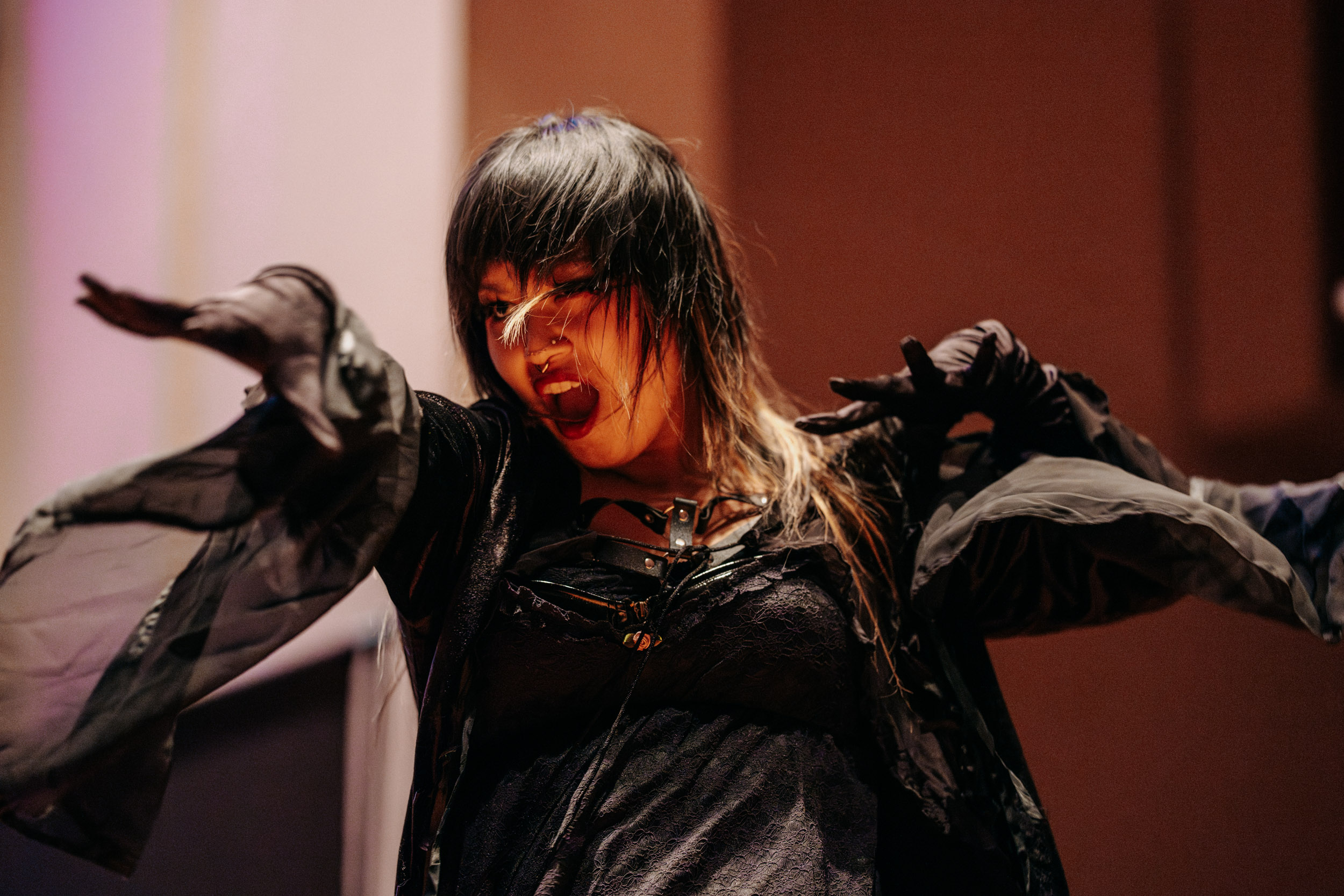 Performer in dramatic costume expressing movement on stage at the Queer Open Mic (QOM) hosted by be; community in Bridgewater, Massachusetts