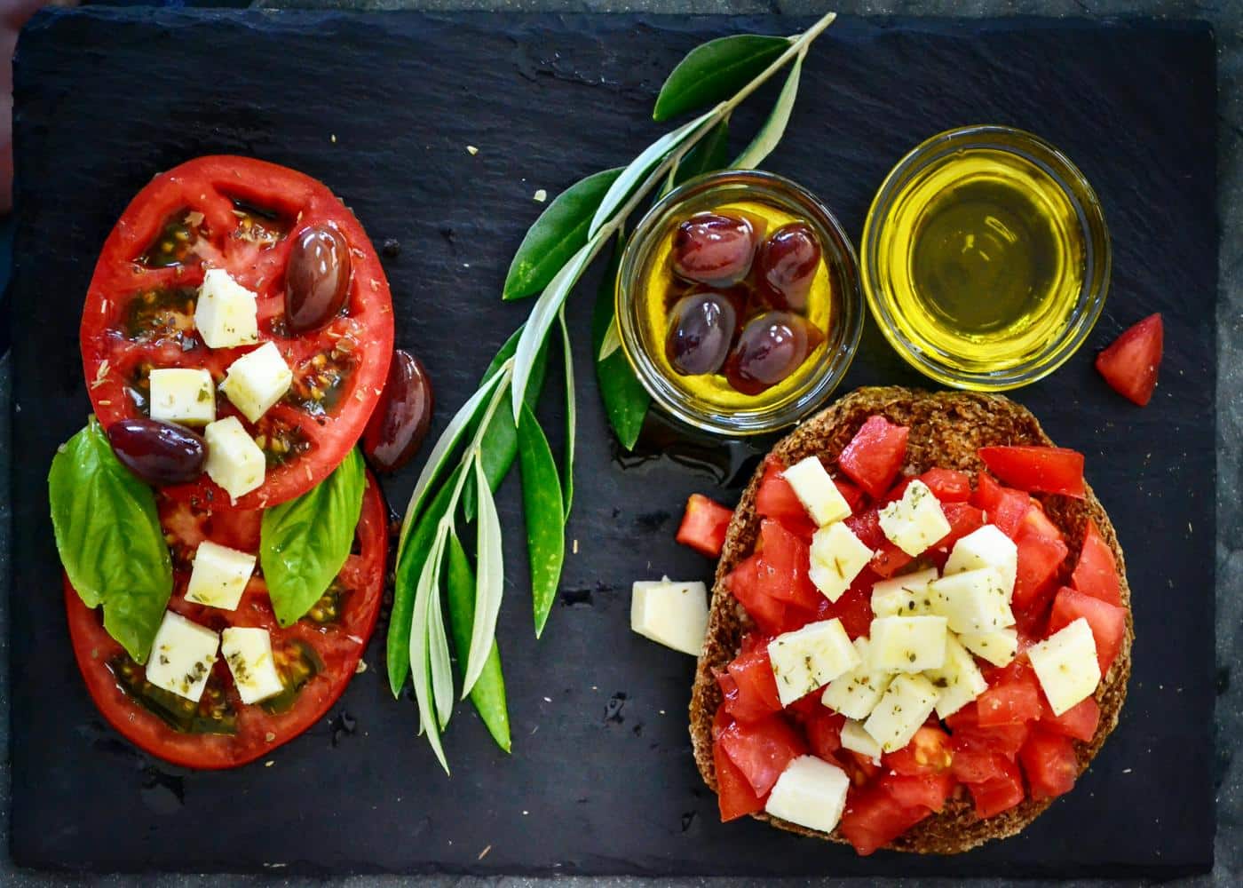 Tomatoes with cheese on top next to olive oil and olives to showcase the mediterranean diet