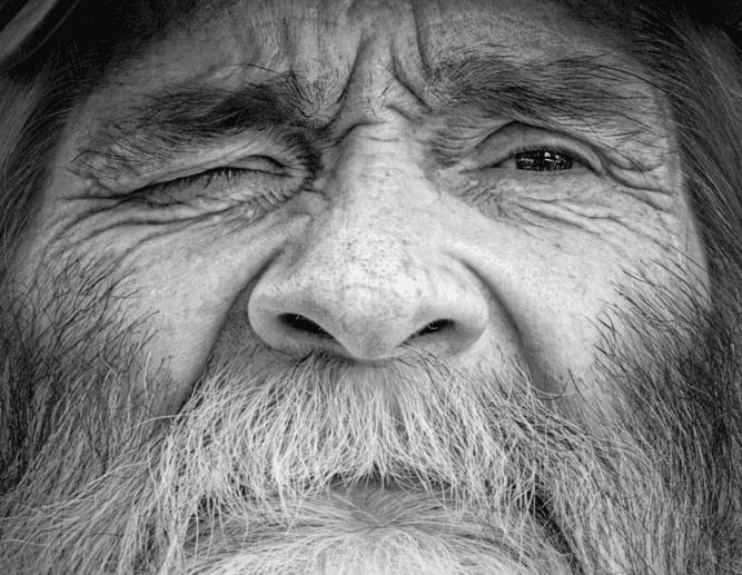 Close-up portrait of an elderly man with a long white beard and deep facial lines, gazing directly at the camera