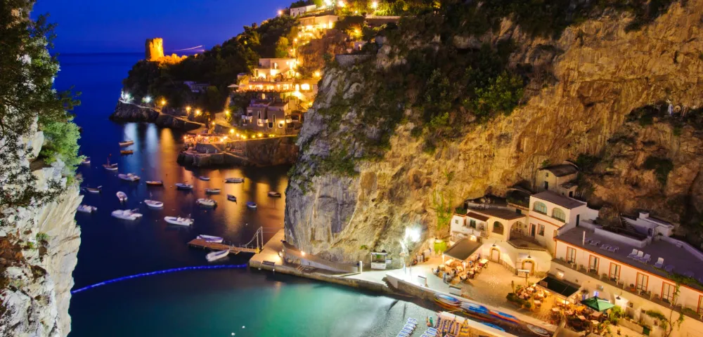 Positano lit up at night, with boats moored in the bay below.