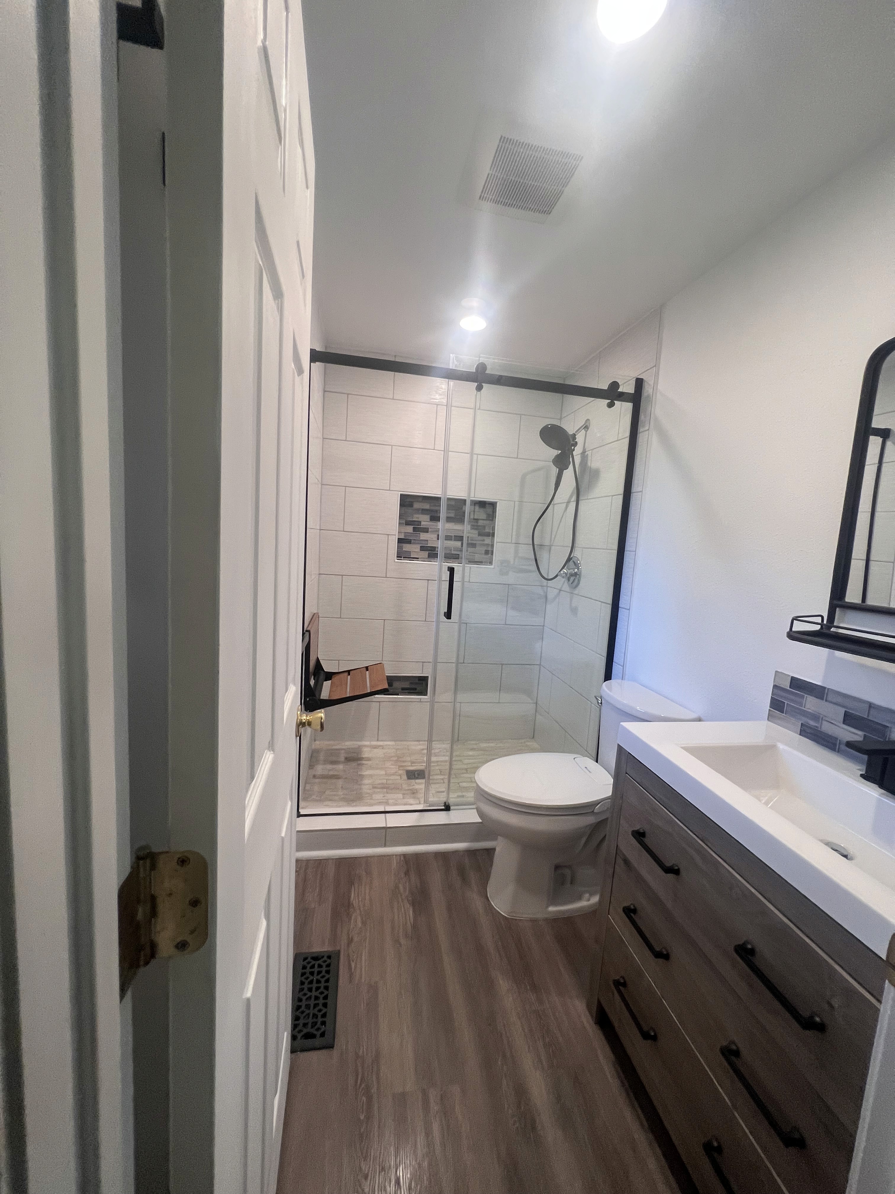 A serene outdoor seating area with two chairs, surrounded by lush greenery and a glassed-in structure.