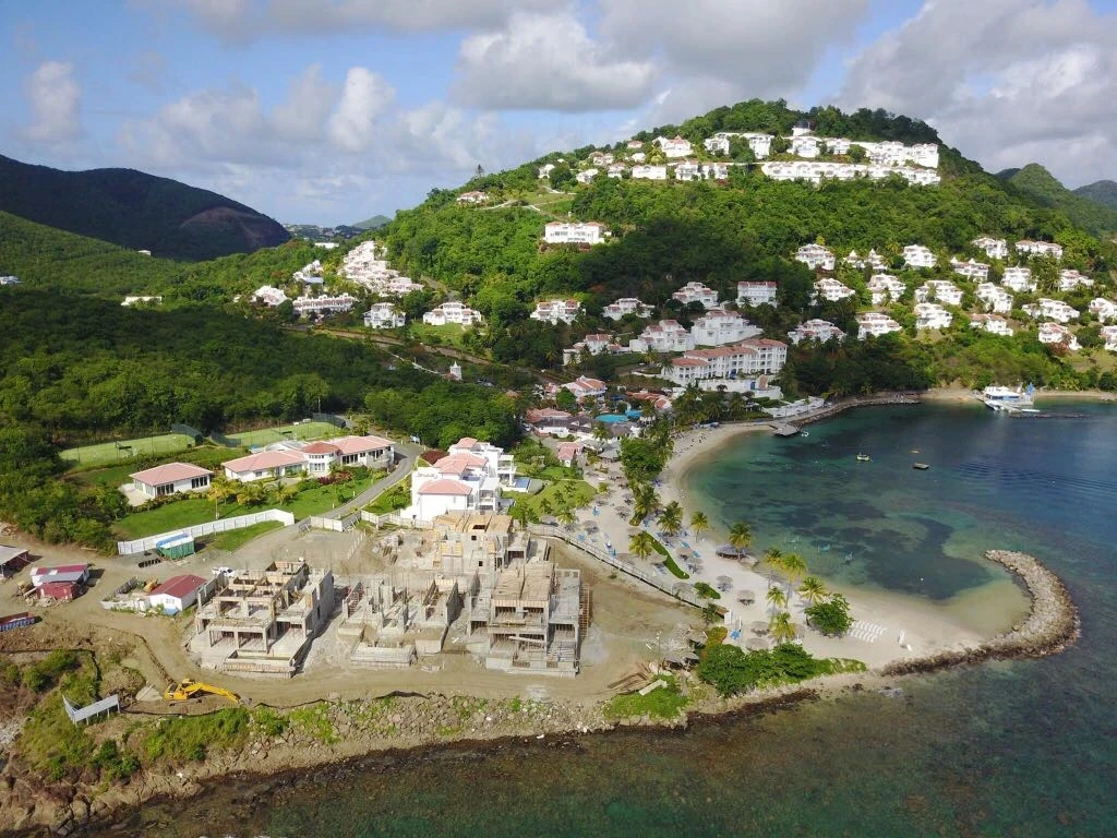 Aerial view of Windjammer Landing Resort villa expansion under construction on a beachfront point in St. Lucia, with hillside villas in the background.