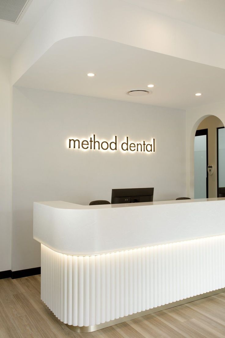 Illuminated “method dental” logo wall sign behind a curved white reception desk in a modern dental clinic interior.