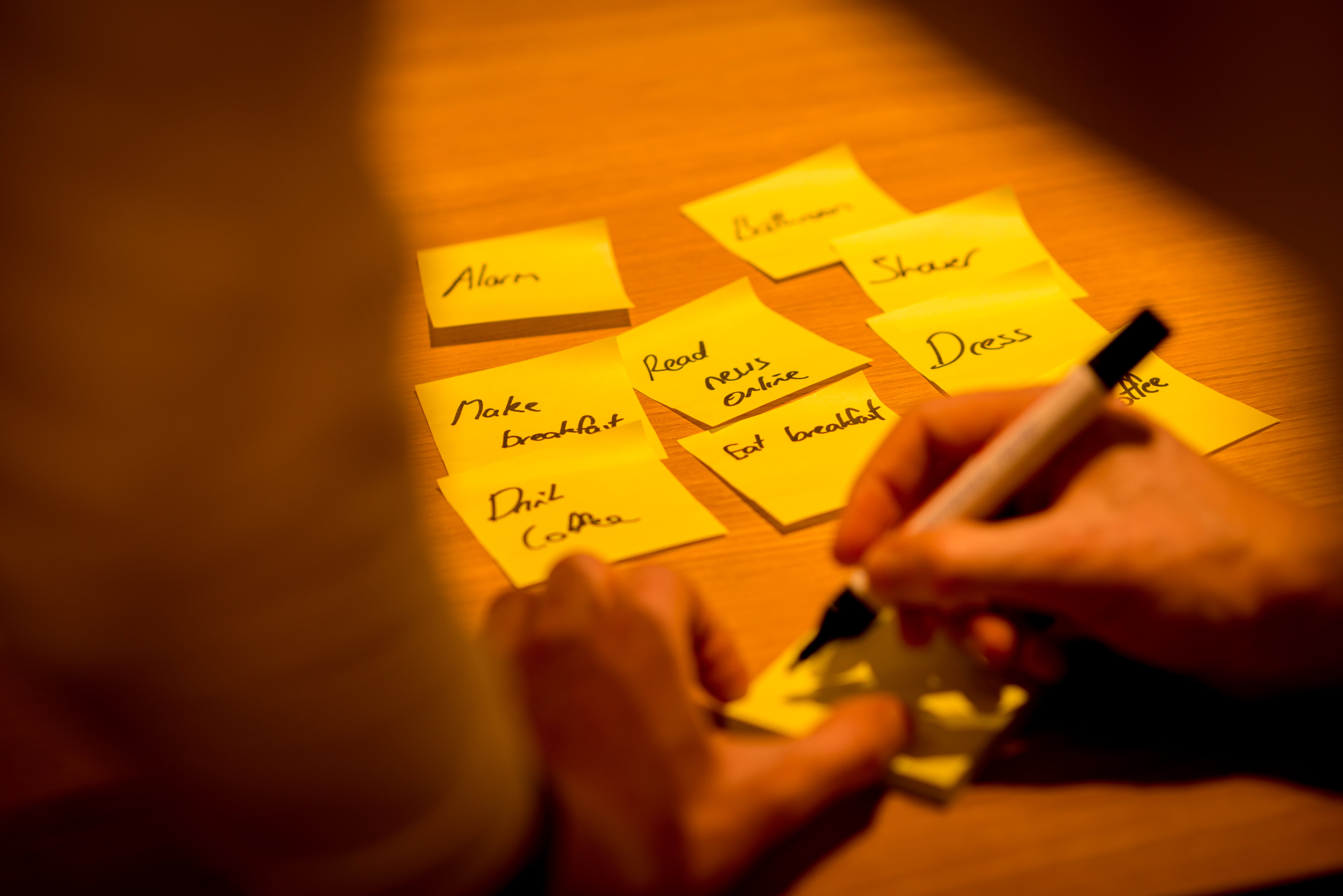 Close-up of hands writing individual ideas on yellow sticky notes for anonymous brainstorming