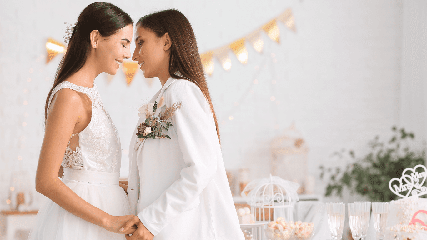Two women in elegant attire lean towards each other, sharing a tender moment in a beautifully decorated space.