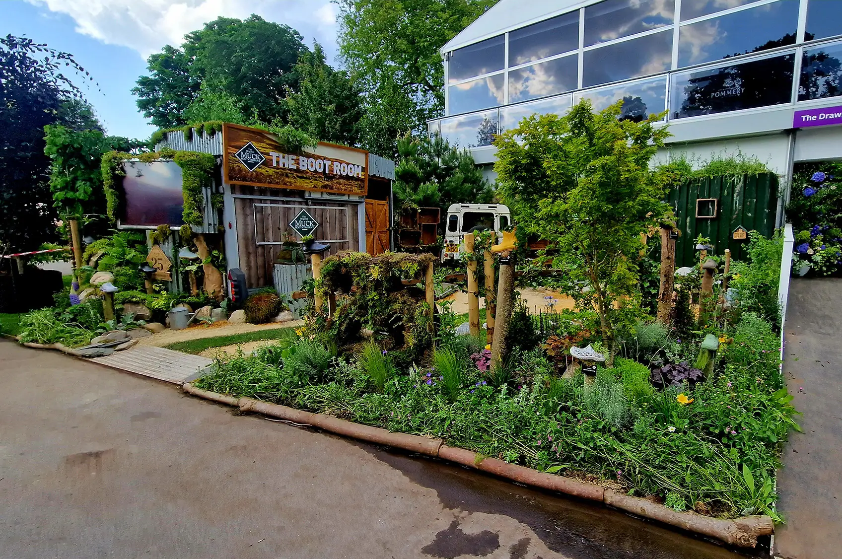 Vibrant garden scene with various plants and trees, a pathway, and a structure in the background under clear blue skies.