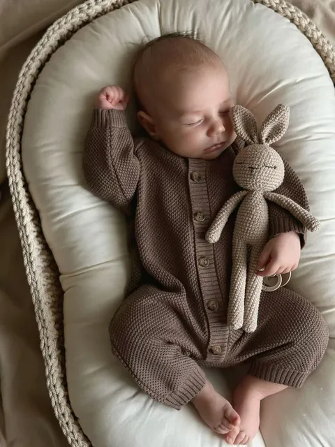 Sleeping newborn in a brown outfit beside a toy rabbit