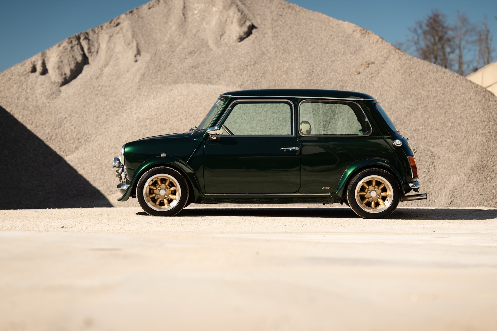 A small, green and black vehicle parked on a sandy surface, with a warm sunset lighting the scene.
