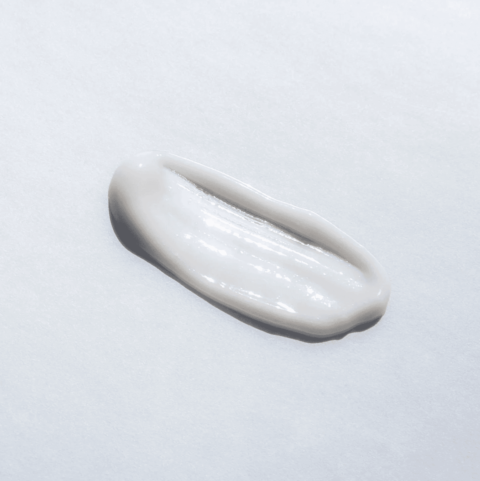 Swirl of white skincare cream on a pale background.