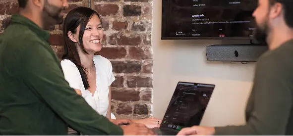 Cogent team members collaborating in a meeting room with a laptop and presentation screen in the background.