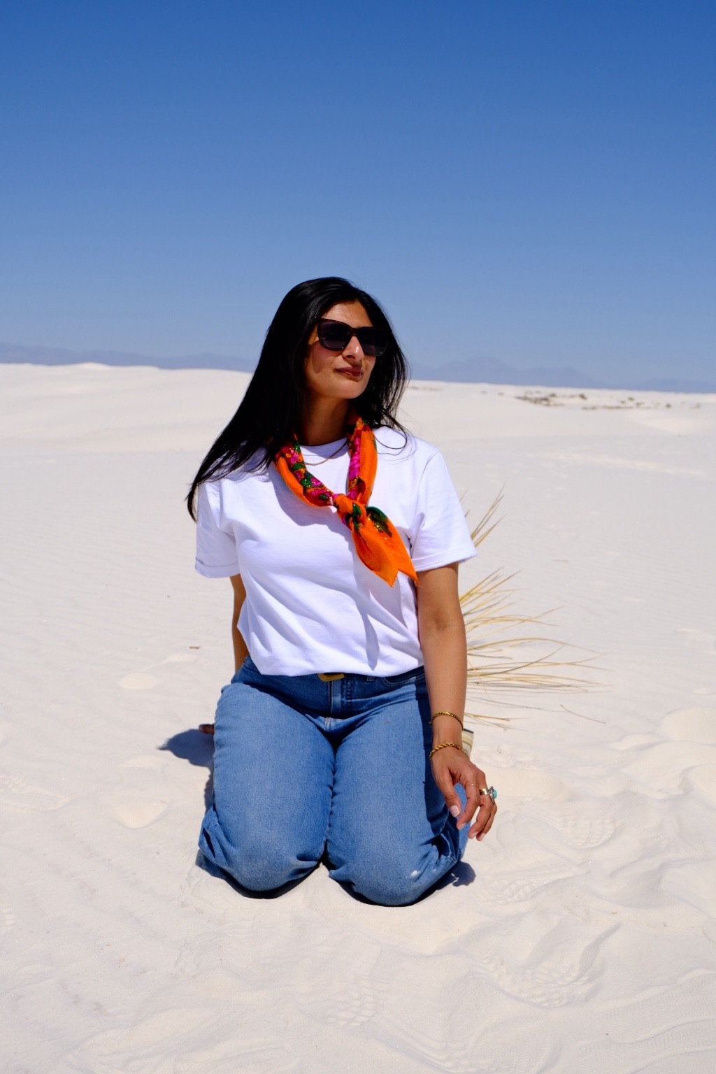 Pranjali at White Sands, wearing a white T-shirt and orange scarf against pale dunes and a blue sky.
