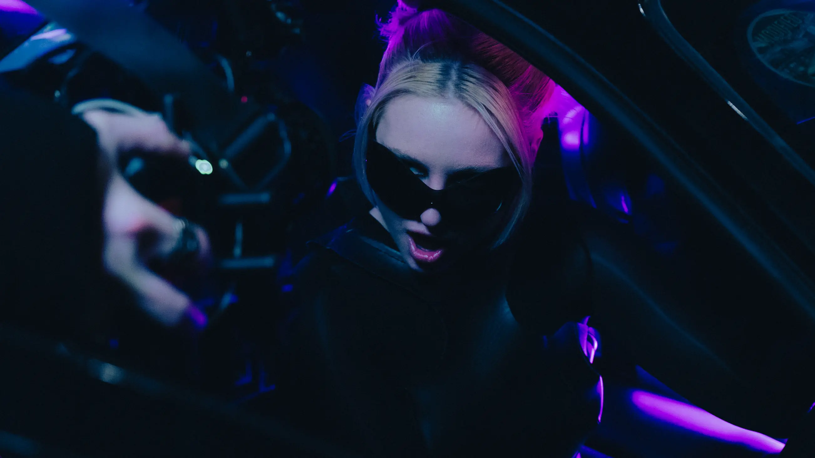 A girl with sunglasses on sitting in a car looking shocked