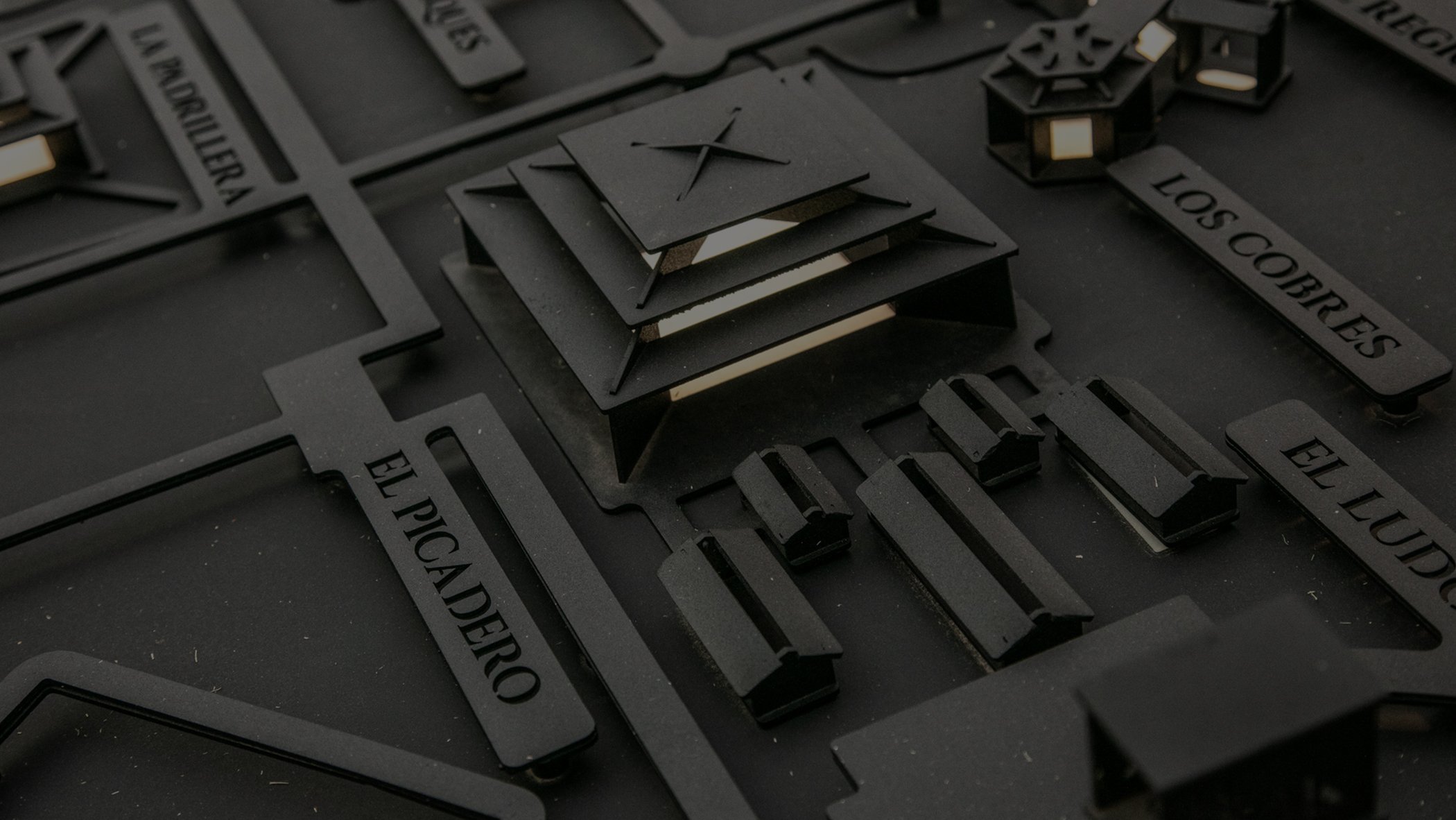 A detailed miniature architectural model featuring layered, black geometric structures labeled with Spanish names like "El Picadero" and "Los Cobres."