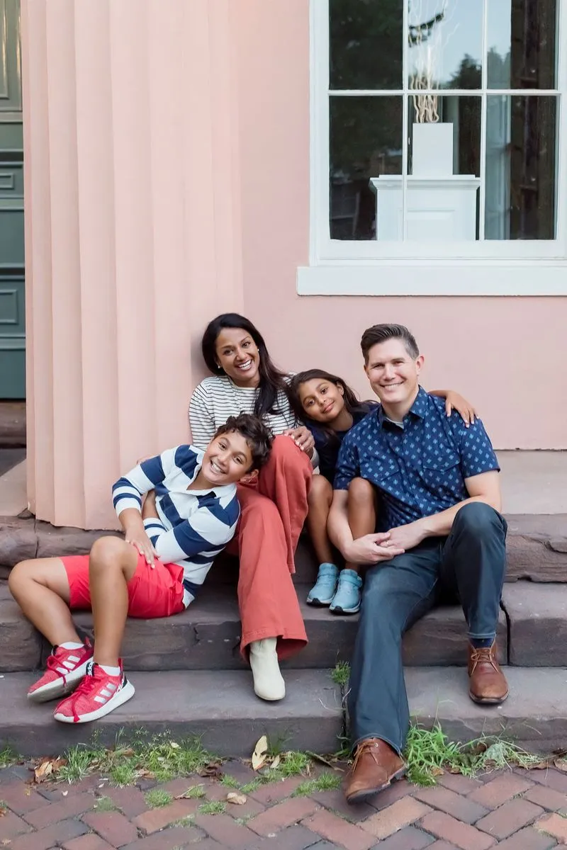 Dr. Rai and her family sitting on steps outside a building, smiling and posing for the camera.