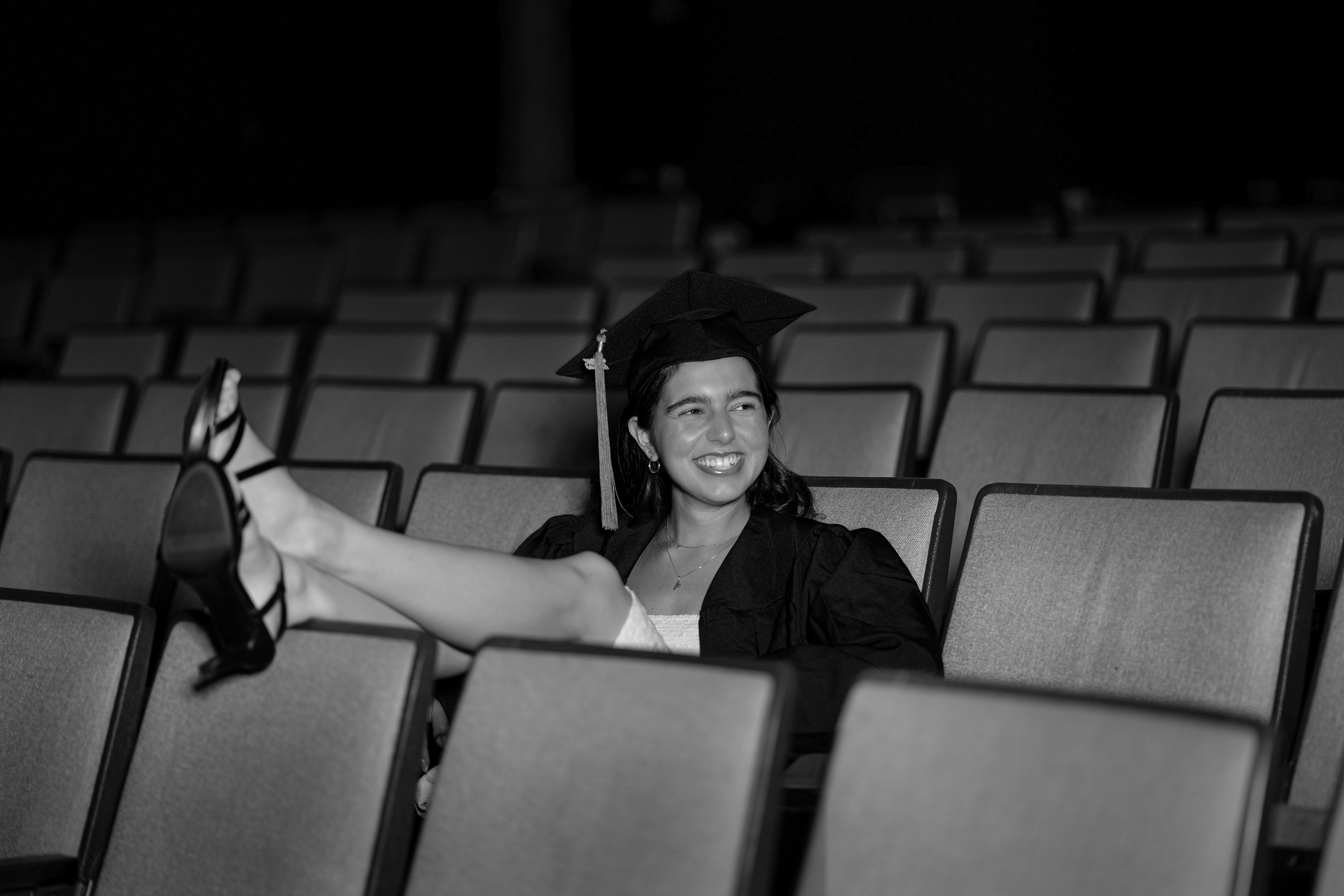 Black and white portrait of woman smiling in empty theater chairs – professional grad photography in Claremont CA. | FFotos
