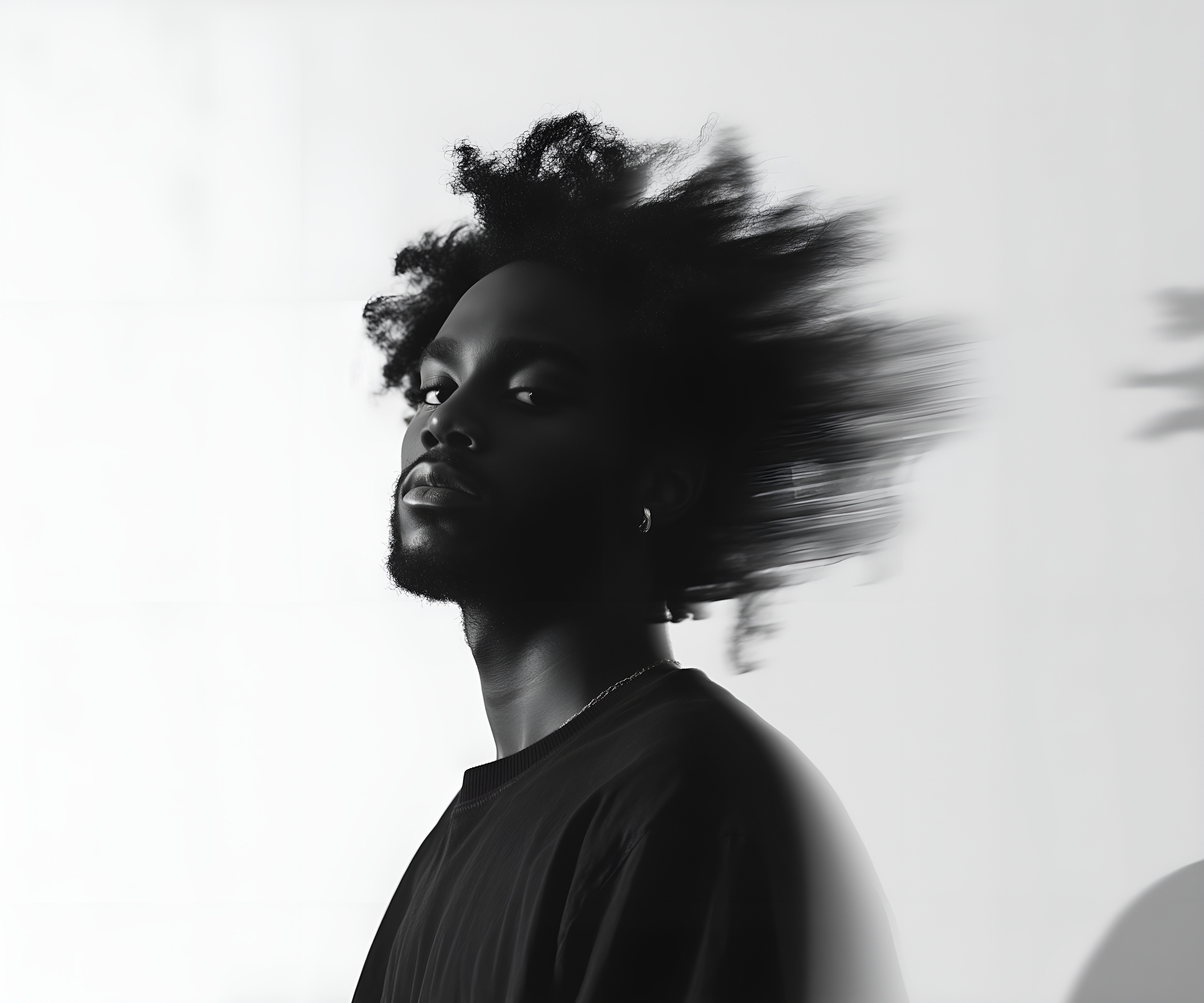 Black-and-white portrait of a man with an afro in motion, wearing a hoop earring and chain necklace, against a light gray background.