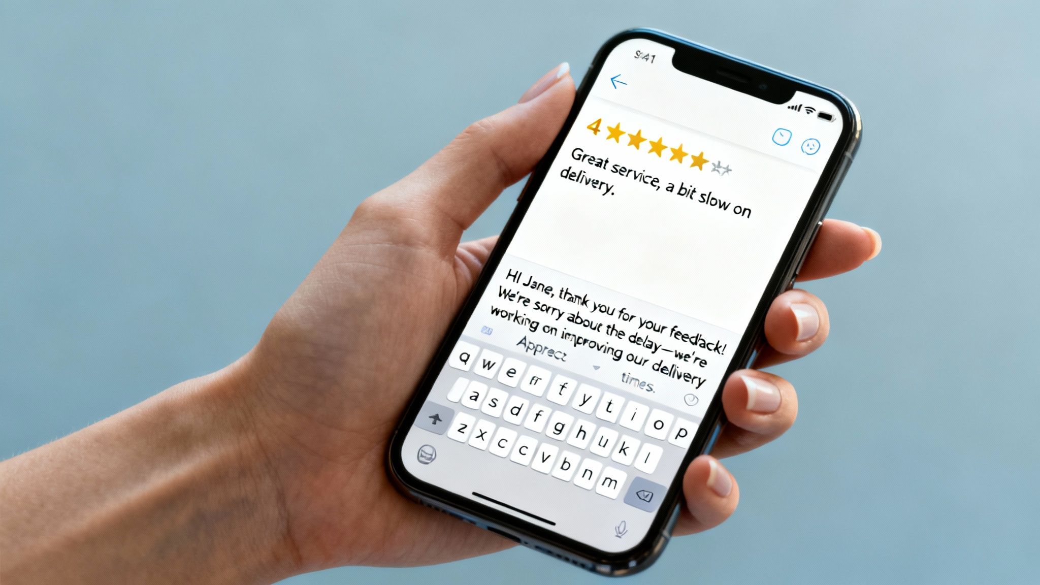 A hand holds a smartphone displaying a 4-star customer review and a company's professional reply.