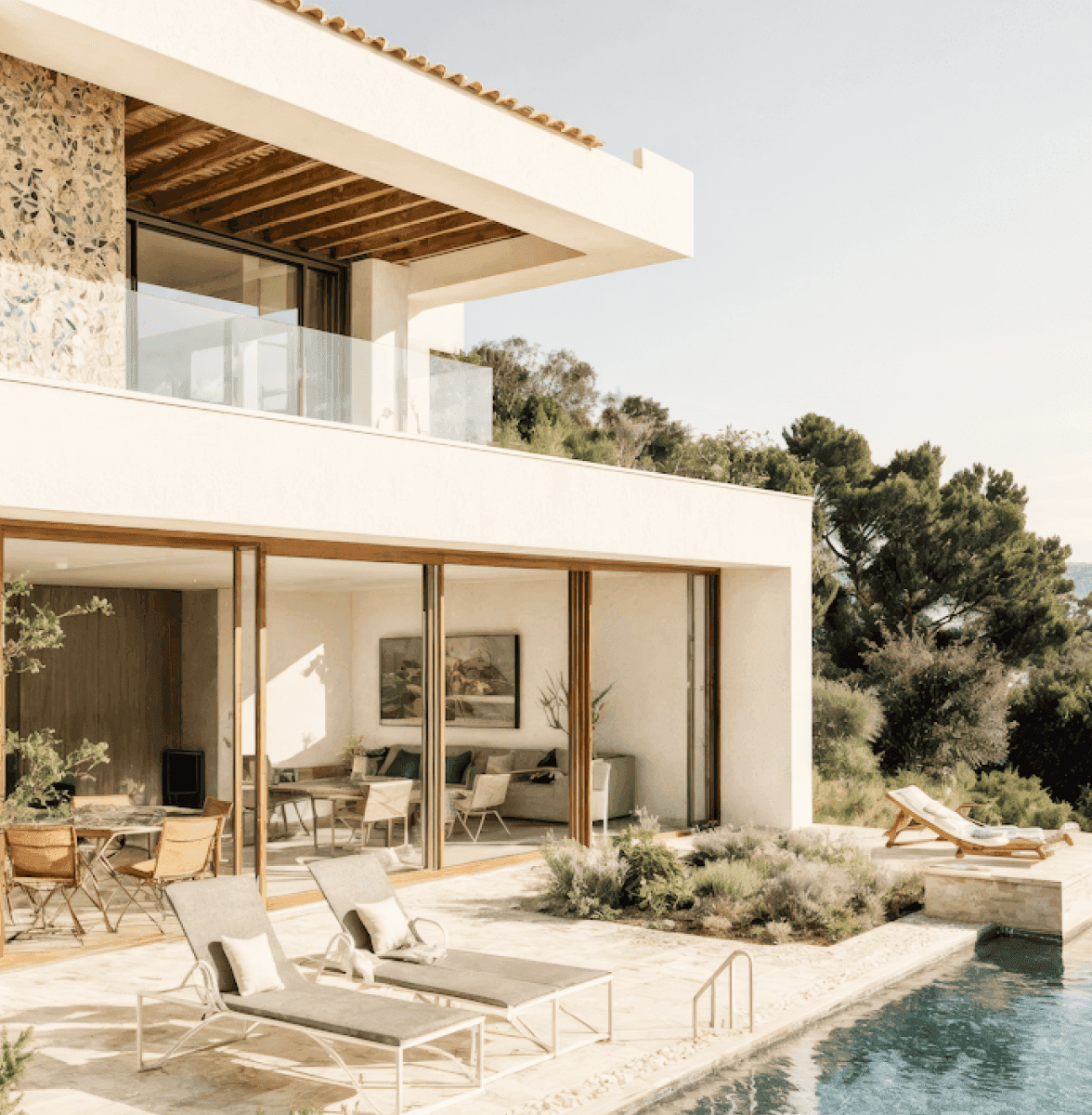 Modern villa with pool, sun loungers, and large glass doors in a sunny setting.