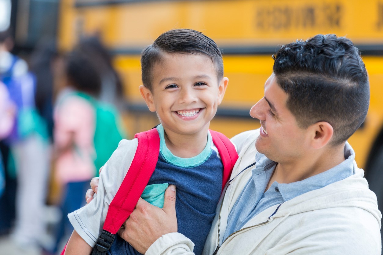 A father and son by a school bus smiling