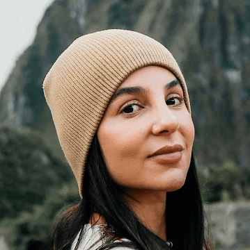 Smiling young woman with curly hair sitting at a laptop, in front of a teal wall.