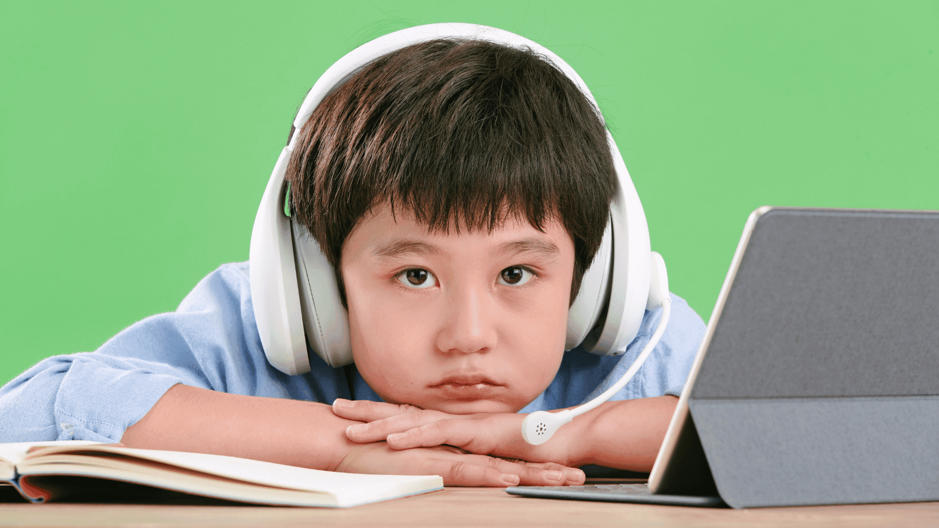 A boy sitting at a desk in front of a tablet, wearing headphones and looking frustrated while listening to HushAway®’s Sound Sanctuary to help him calm down.