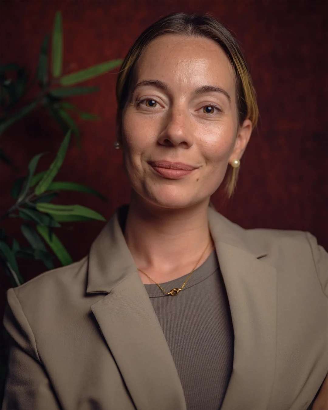 A confident person with short, styled hair and a leather jacket poses against a dark backdrop.