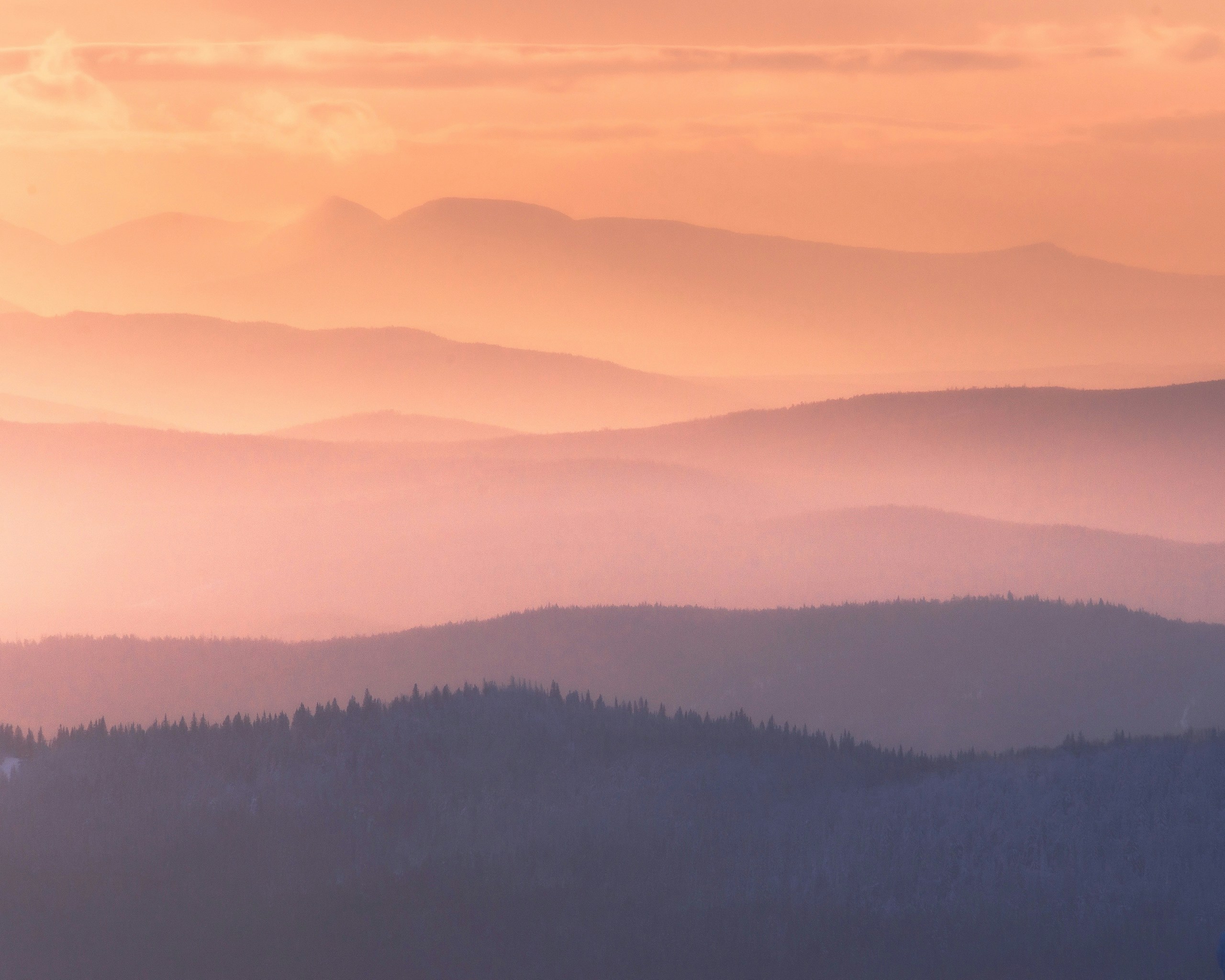 Hazy mountain layers at sunrise with orange sky.