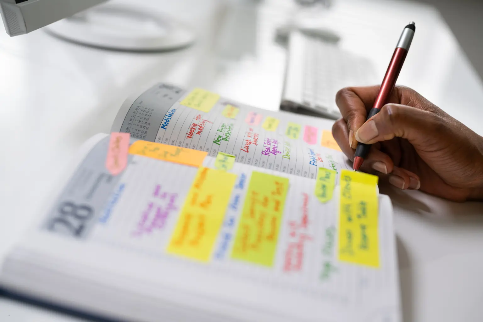 Automated calendar systems planner filled with colorful sticky notes and a person writing tasks with a red pen