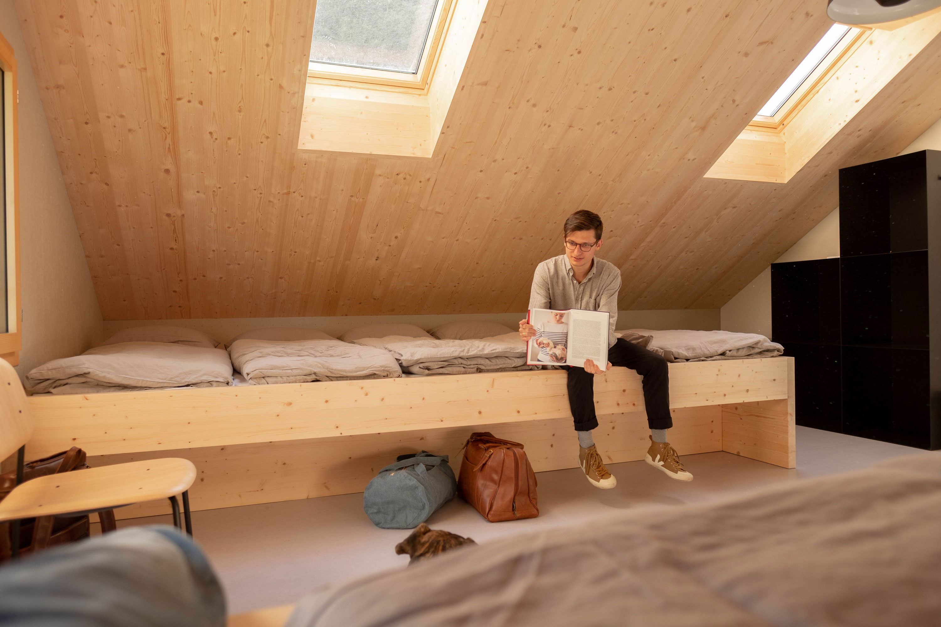 Foto Mensch sitzt auf dem riesen Bett, warmes helles Holz, jetzt buchen