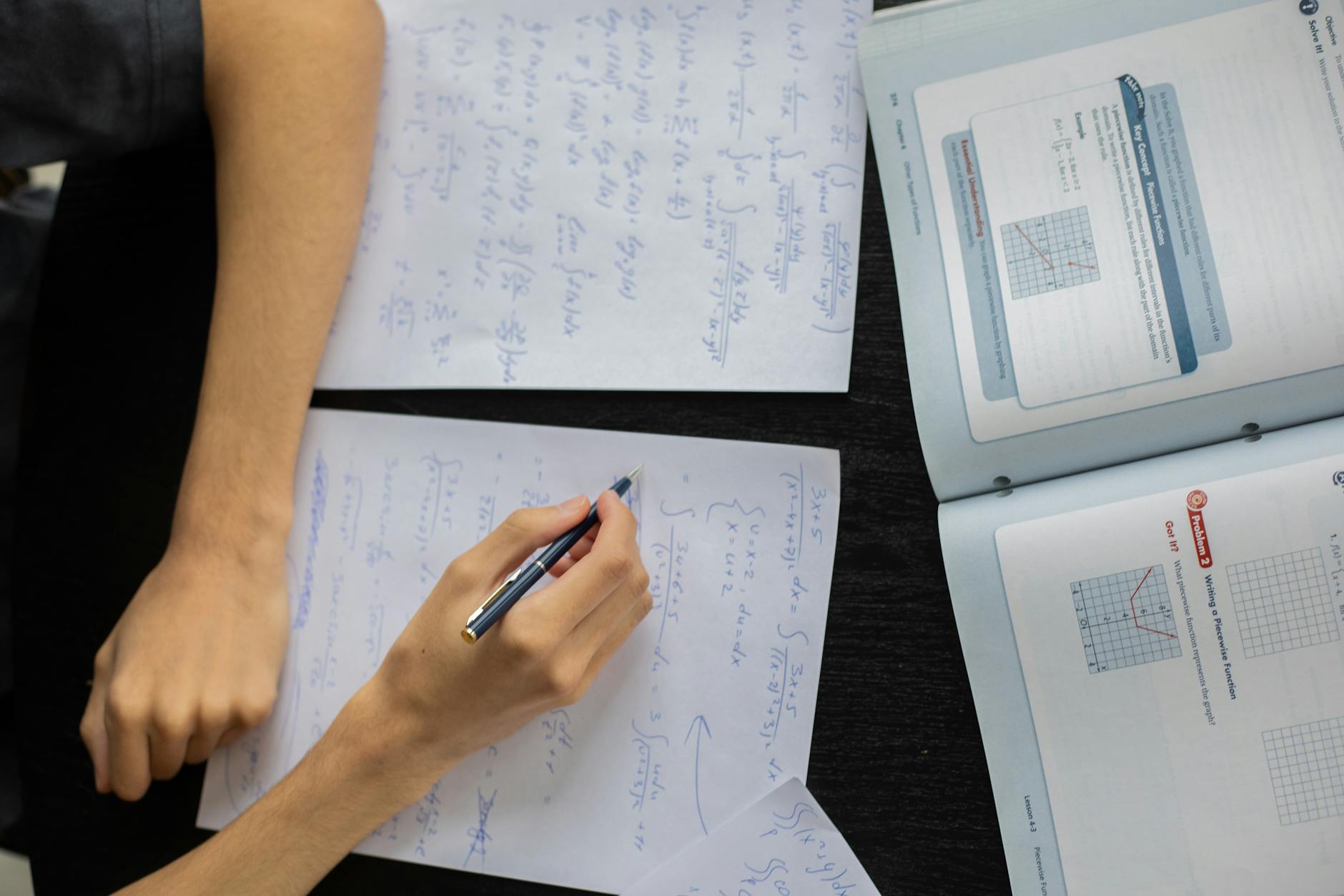 Close-up of a wooden desk featuring an open textbook, a highlighter, and a notebook filled with lecture notes.