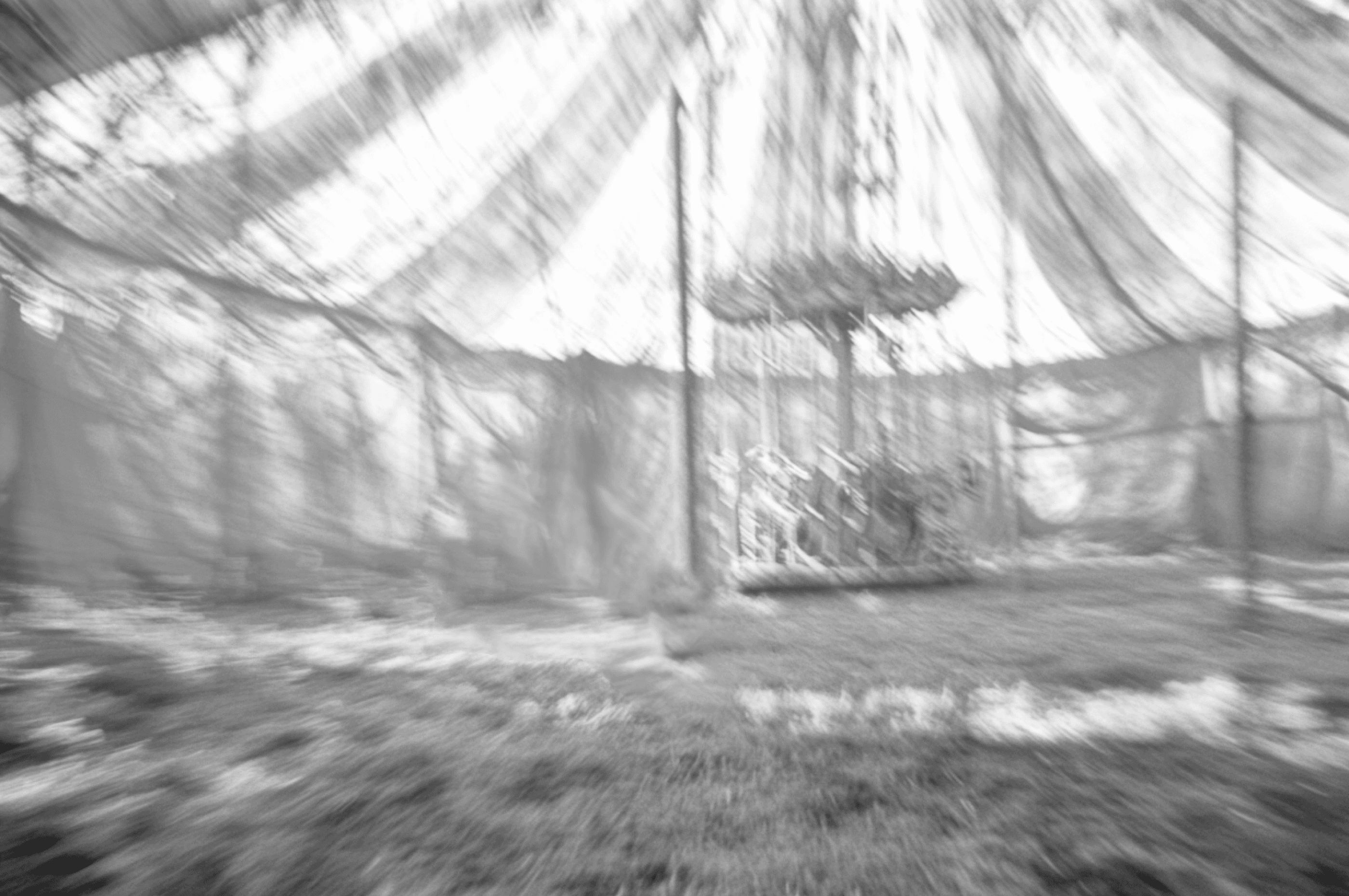 Blurred black and white photo of the inside of a circus tent. A vintage children's carousel is faintly visible at the center, adding a nostalgic, dreamy atmosphere.