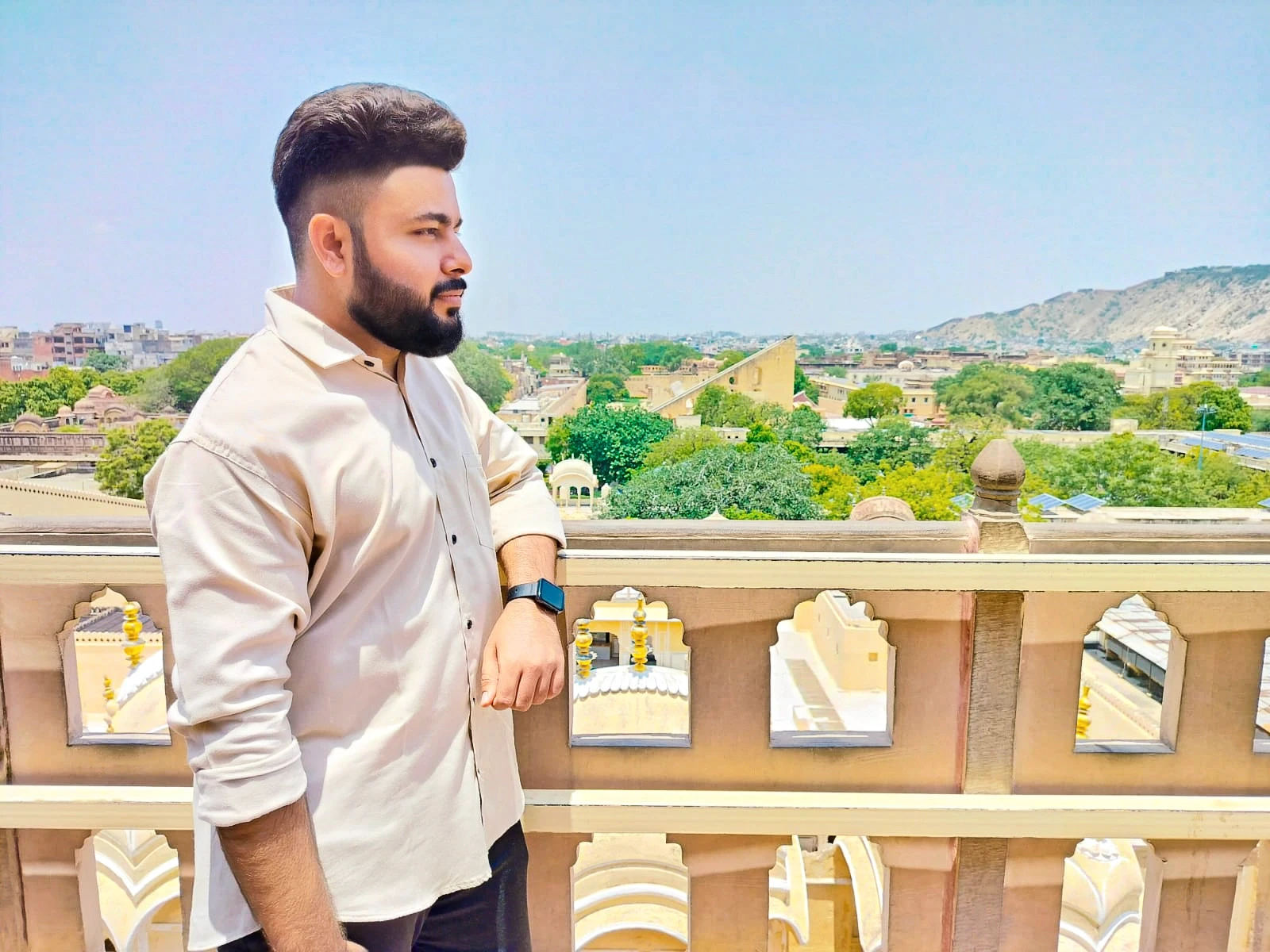 Person wearing a blue puffer jacket and red backpack standing in front of a light blue building on a city street.