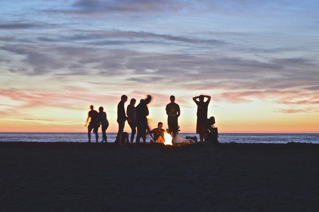 Group of people enjoying a beach bonfire at sunset.