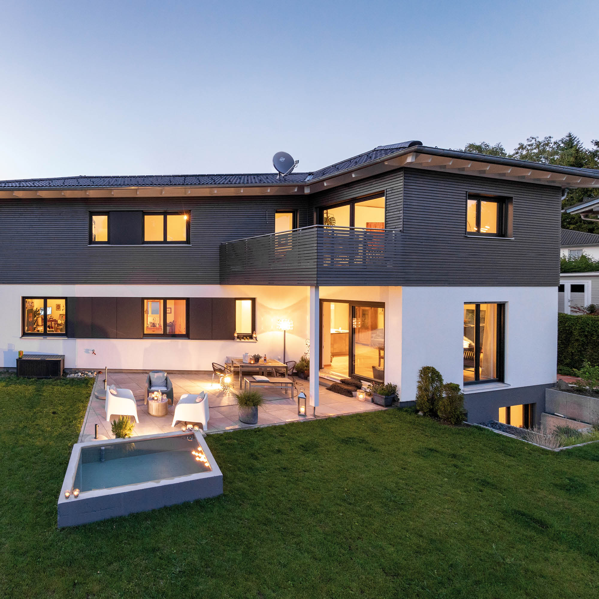 Modernes zweistöckiges Haus mit Terrasse, kleinem Pool und beleuchtetem Garten im Abendlicht.