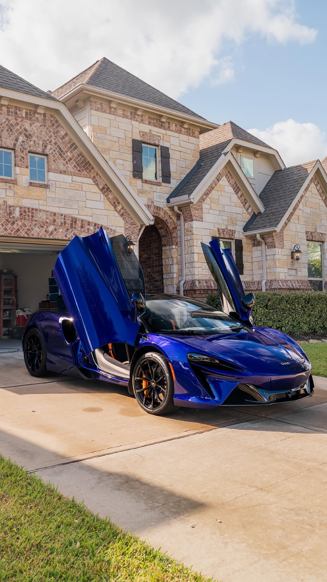 A metallic blue McLaren Artura after a premium exterior detail and hand wash on a luxury driveway in a Houston neighborhood.