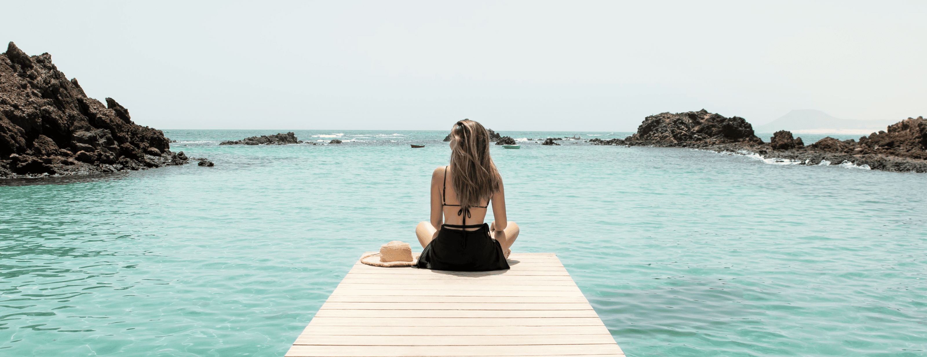 Person sitting on a wooden pier over turquoise water surrounded by rocky cliffs