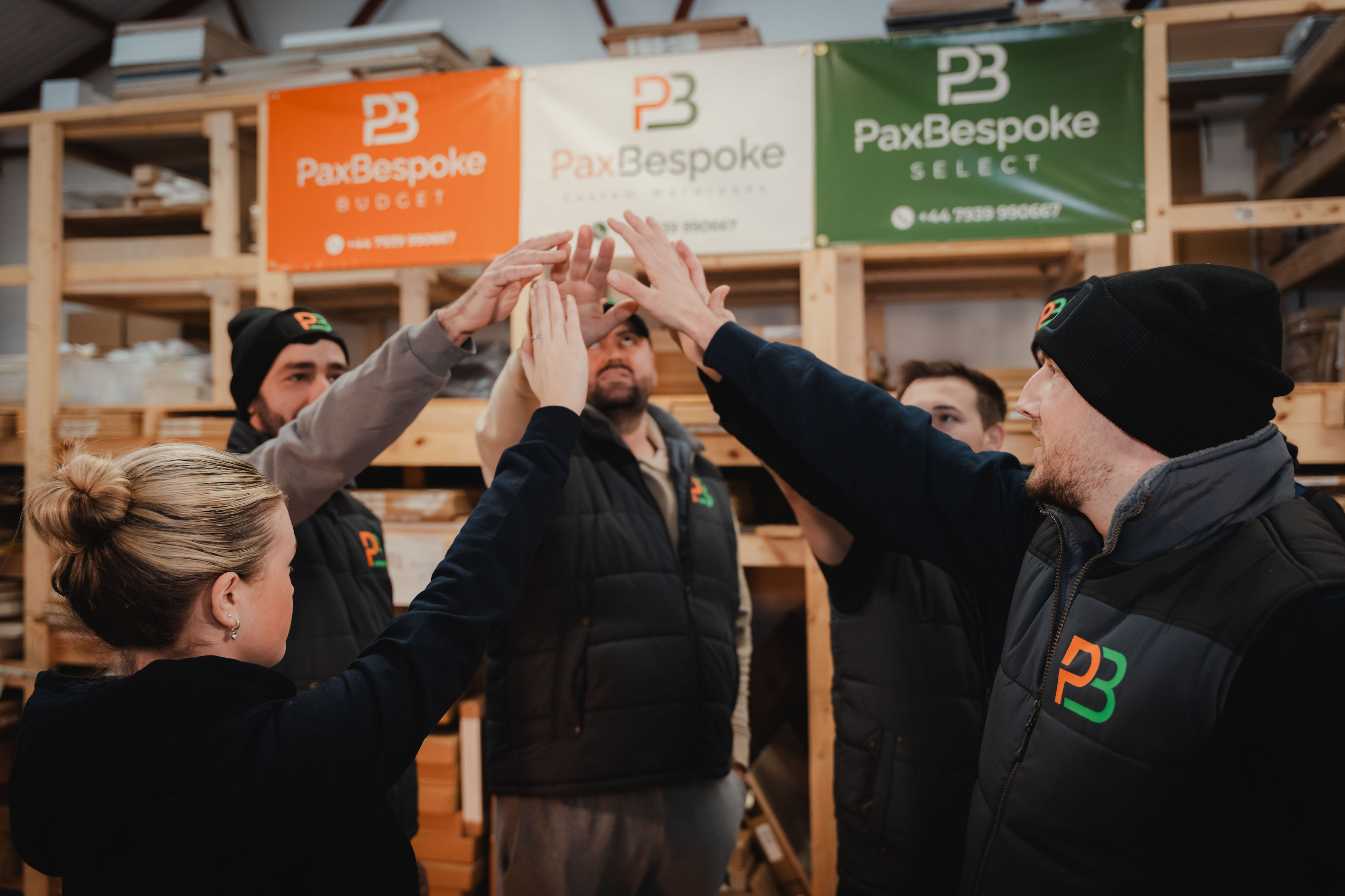 the PaxBespoke team uniting hands in the air in the brand's warehouse