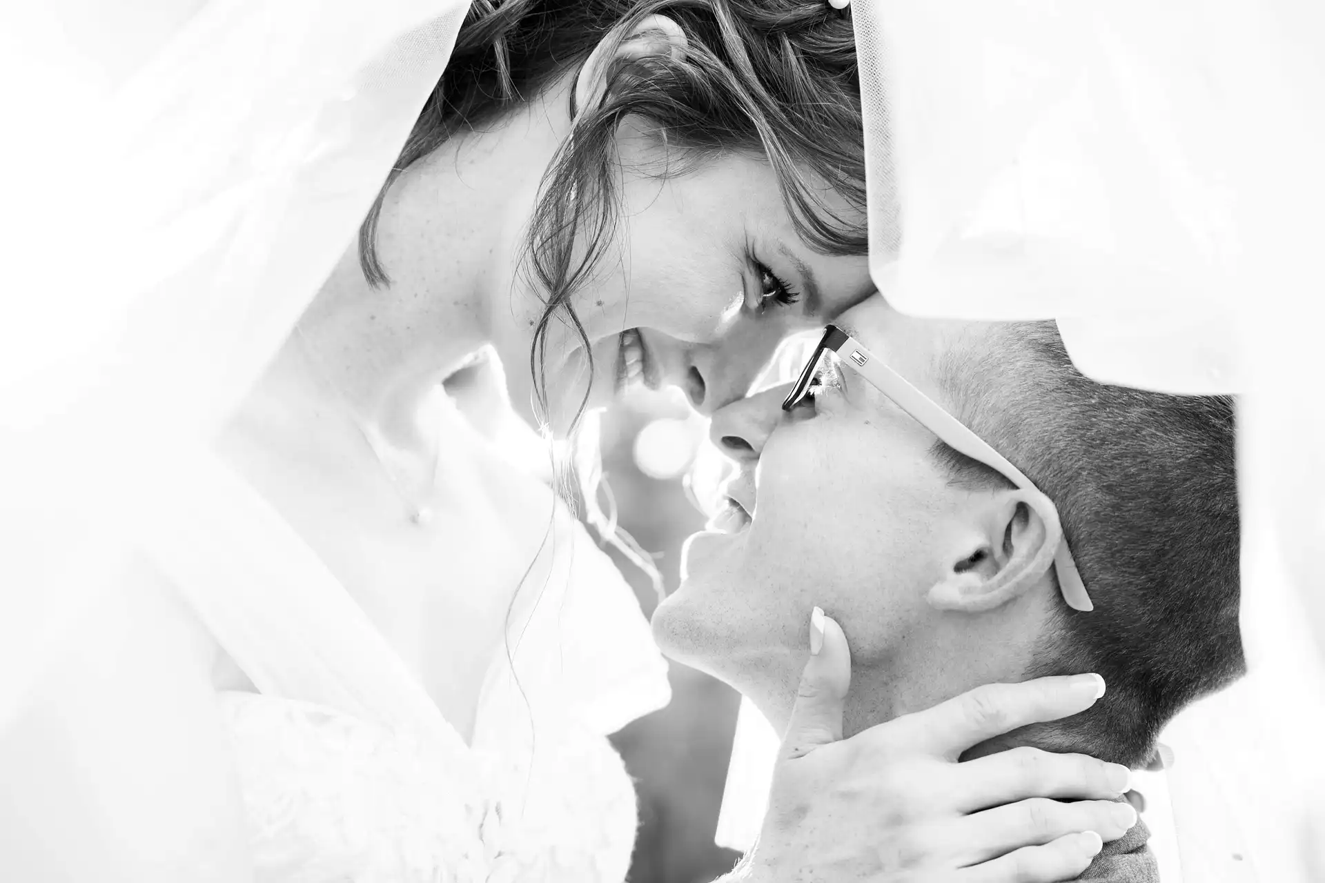  black and white image of a couple gently holding each other's faces under a veil