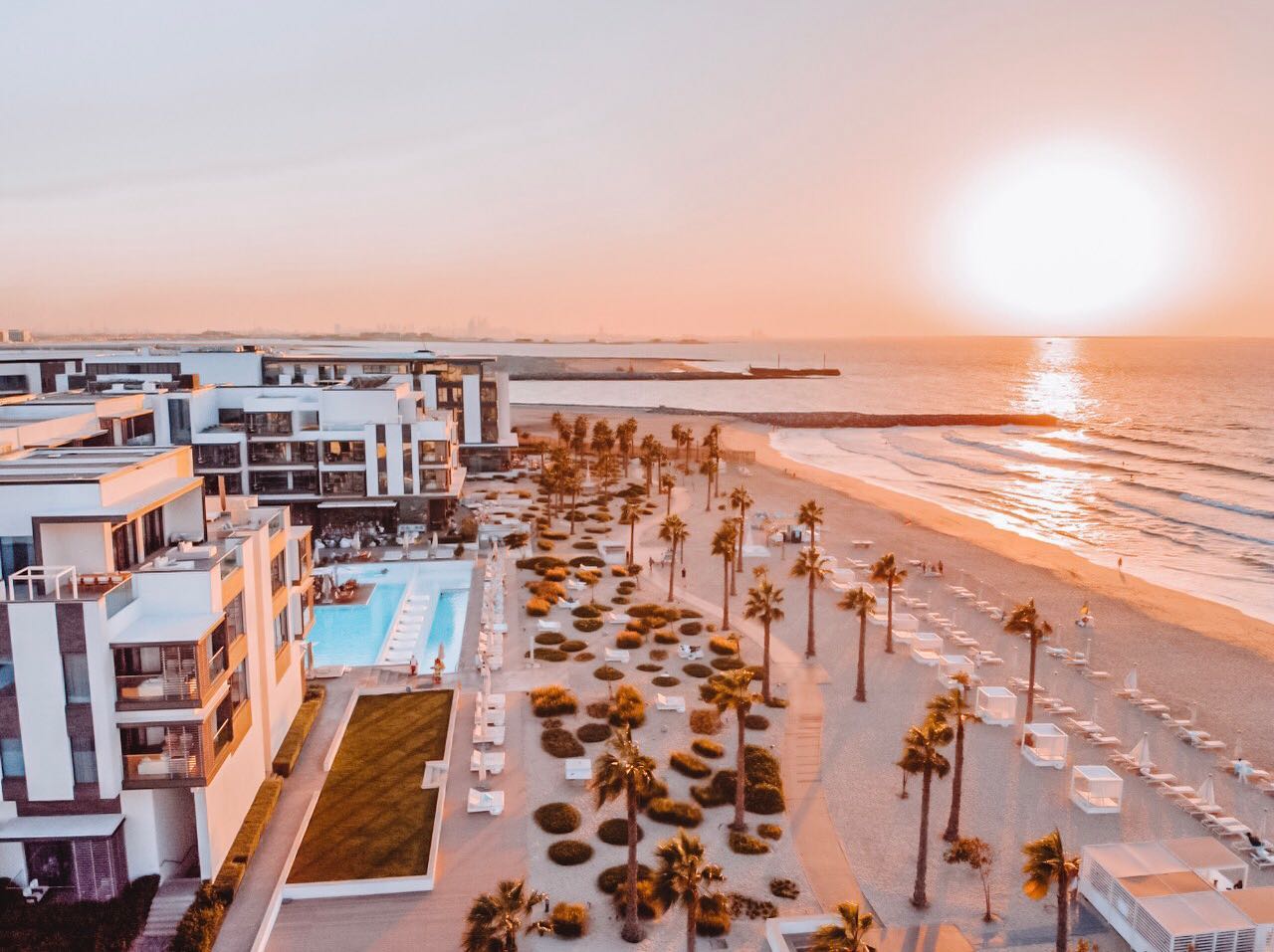 Studio portrait of a woman in a bright blue turtleneck and white trousers standing in front of a bold red square backdrop.