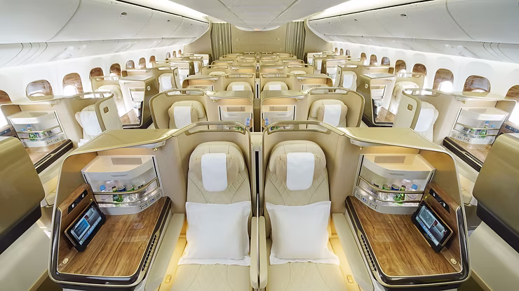 Luxury business class cabin of an Emirates Boeing 777 featuring cream leather seats, wood-grain finishes, and individual mini-bars at every seat.