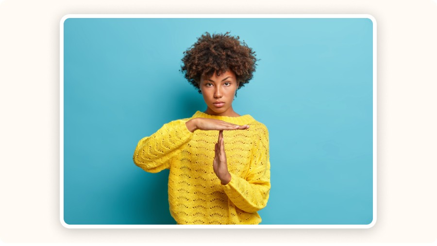 Personne en pull jaune sur fond bleu, faisant un geste “T” avec les mains