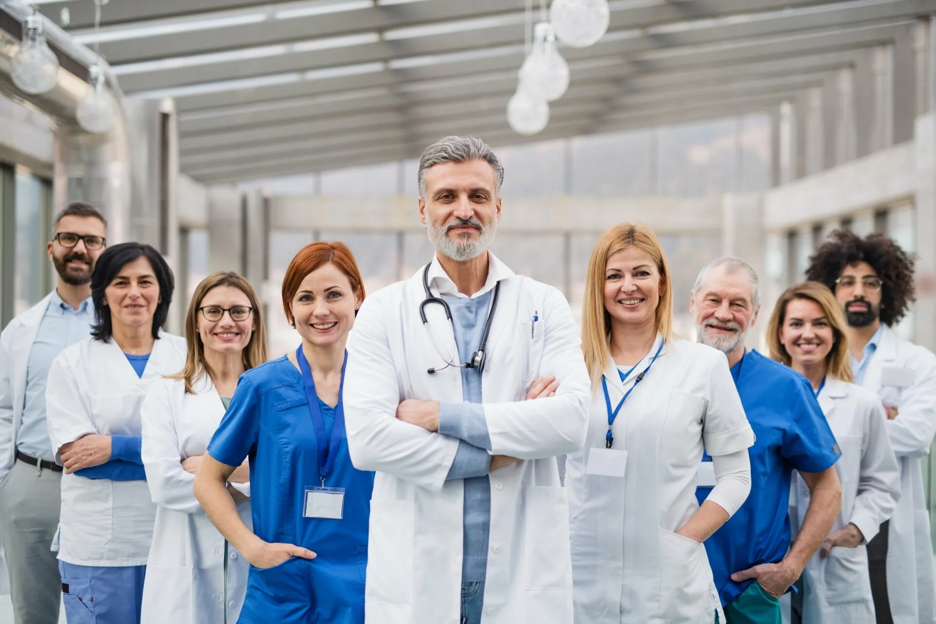 A group of healthcare professionals smiling, wearing scrubs and lab coats, stands together in a clinical setting.