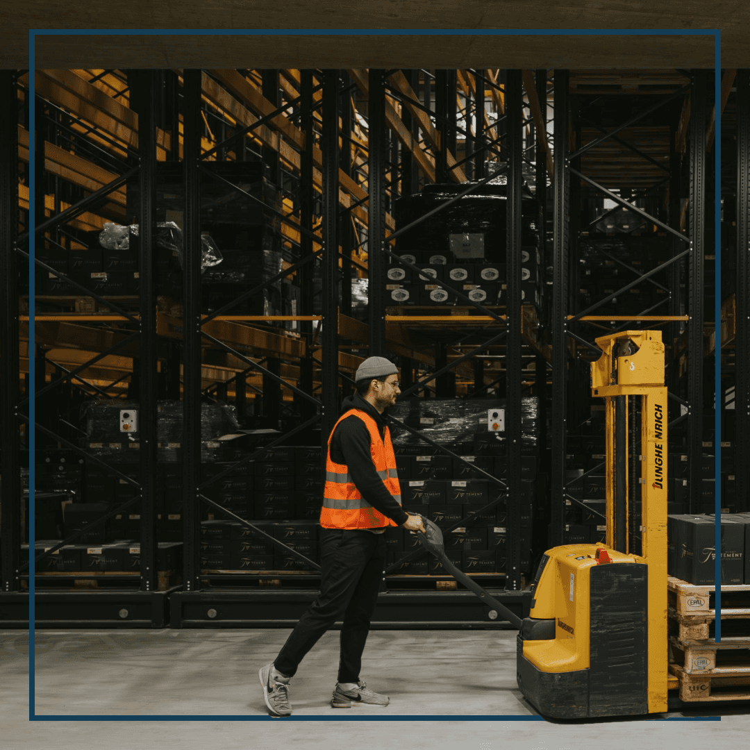 Ein Mann in oranger Warnweste der einen Hubwagen in einem Weinlager bedient