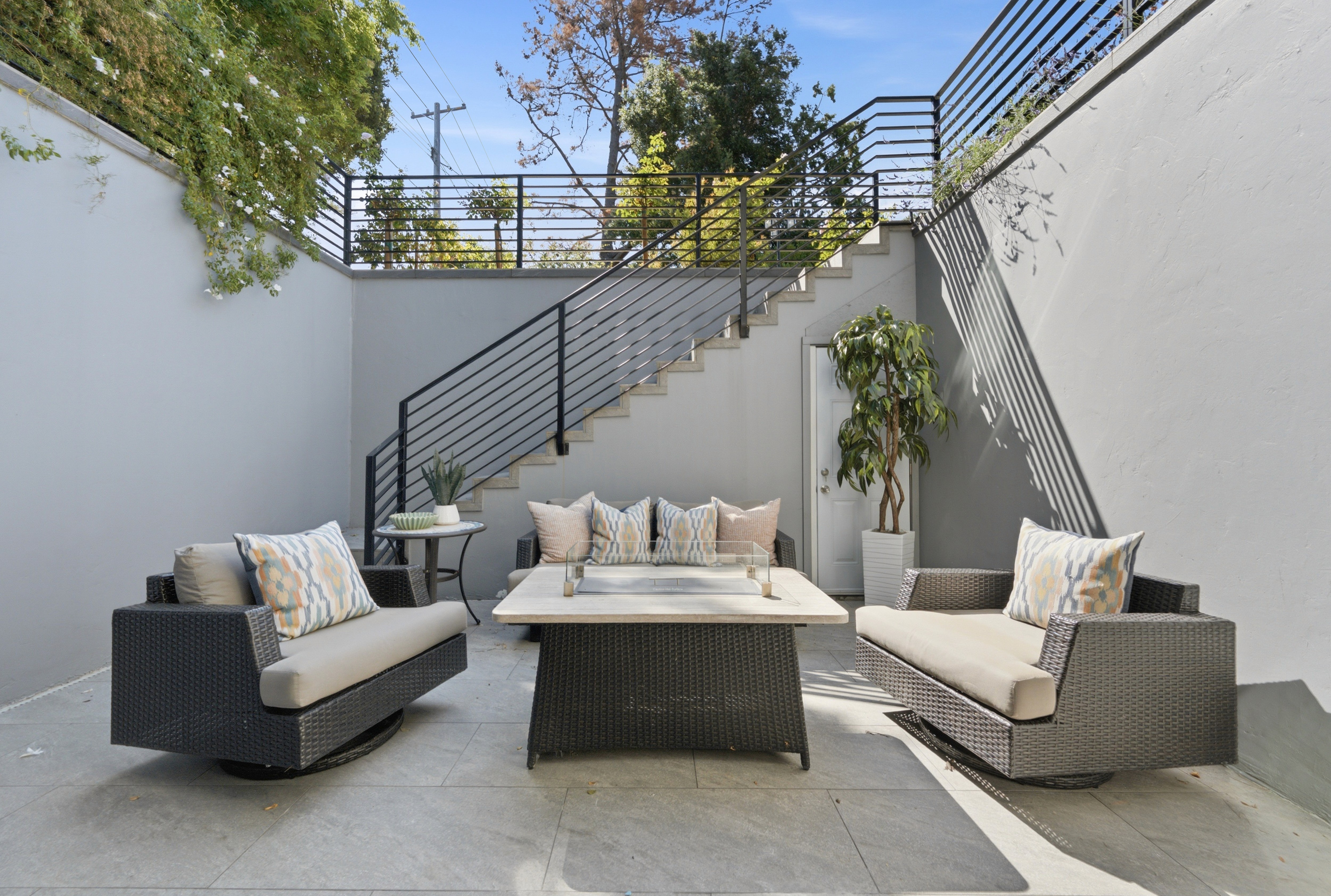 Sunken courtyard with wicker lounge seating, a fire table, and a black metal staircase up to the yard.