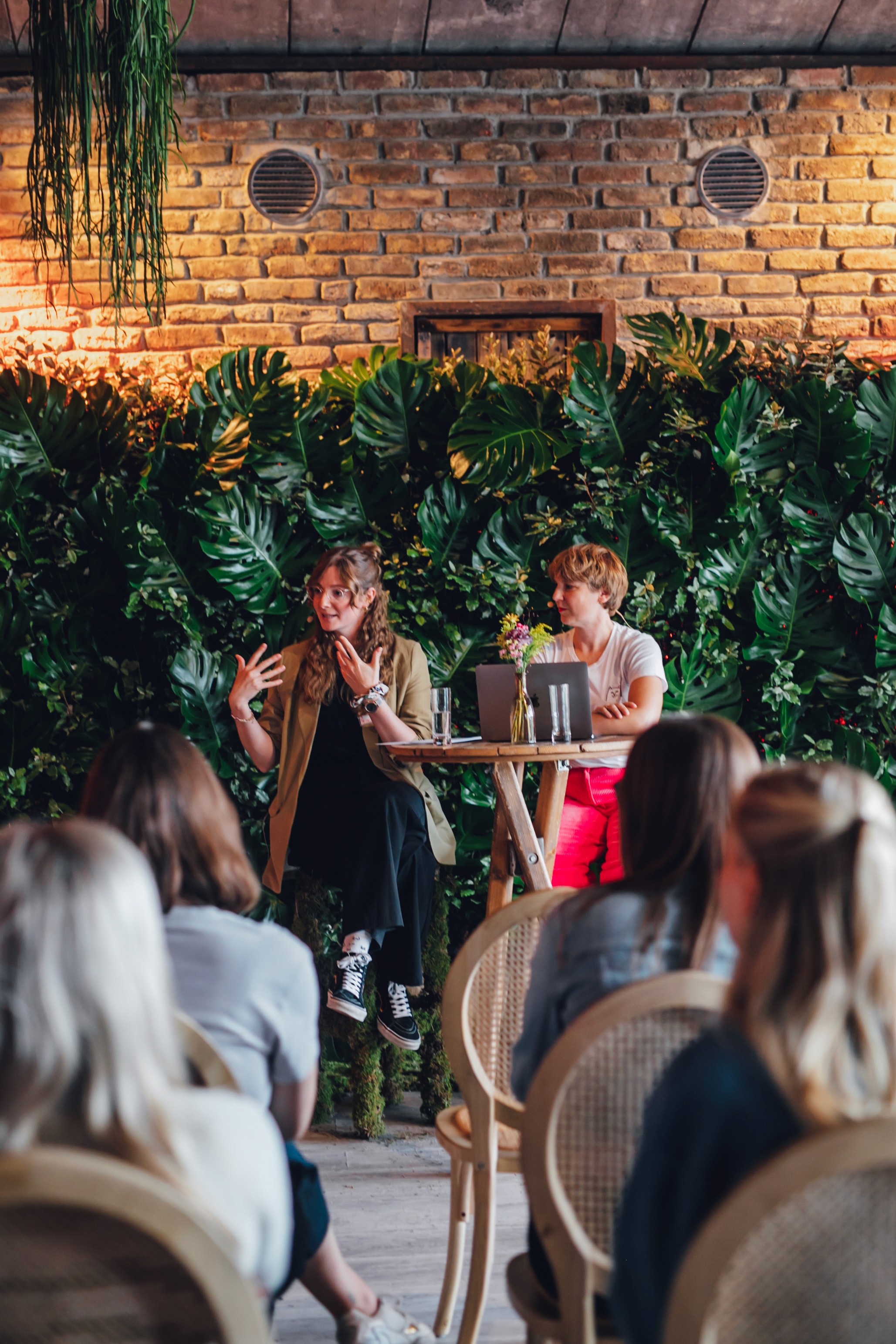 Teilnehmerinnen des Kreativzeit Festivals hören zwei Rednerinnen in einer floralen Kulisse zu.