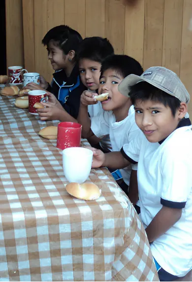 Grupo de niños sonriendo mientras desayunan juntos en una mesa con mantel de cuadros.