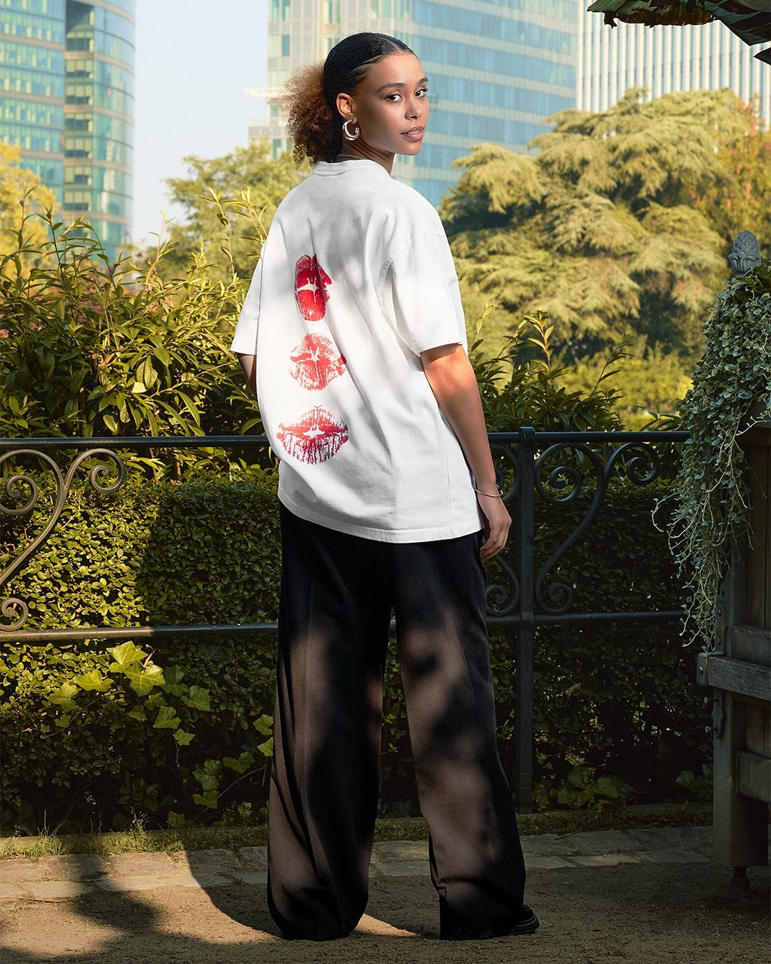 Vue de dos d'une mannequin dans un jardin portant un t-shirt ample blanc imprimé de la marque Arbor Antwerpen
